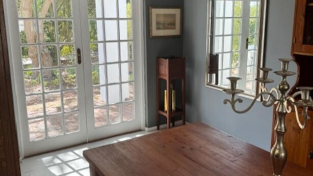 A dining area with a wooden table, a chandelier, and a view through a glass door. - Bordeaux 45 (Cape Town)