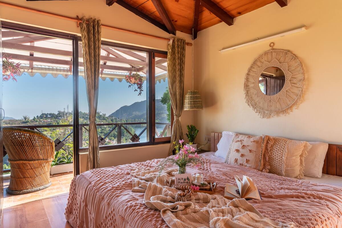 Ein Schlafzimmer mit einem großen Bett, Bergblick, einem Korbstuhl und einer hängenden Pflanze.