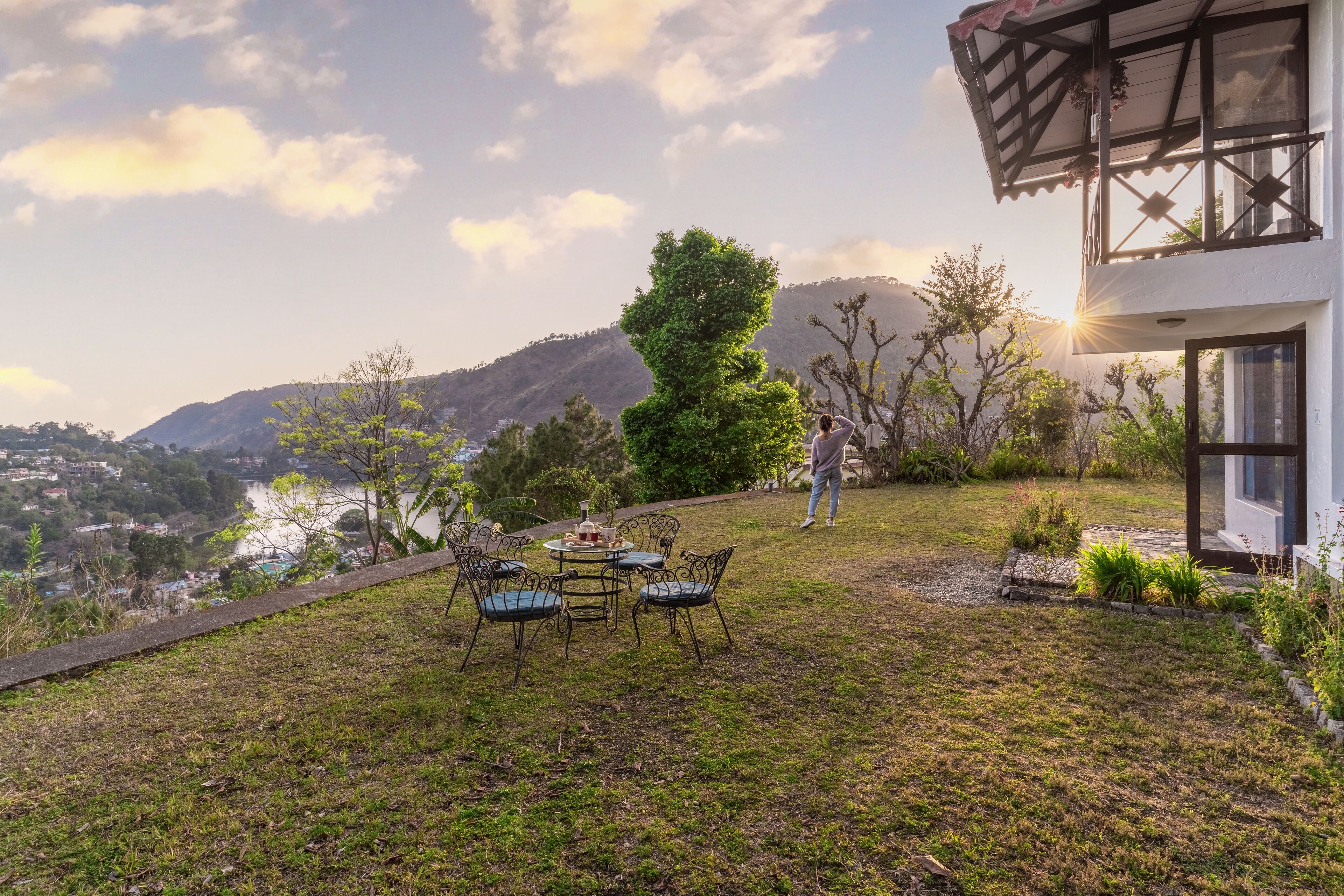 Une terrasse avec une table et des chaises, une personne debout, et une vue sur une vallée et des montagnes.