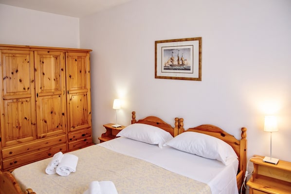 A hotel room with a wooden wardrobe, a bed with white linens, two bedside lamps, and a framed picture on the wall.