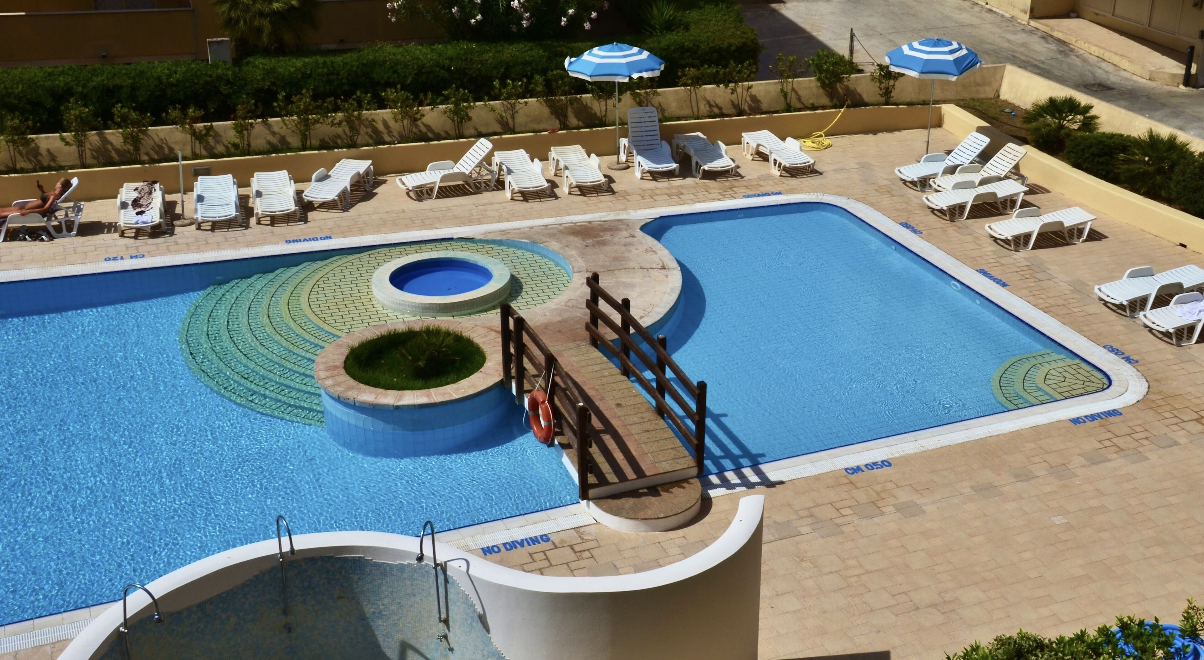 Zona de piscina con múltiples tumbonas, un trampolín y un flotador.