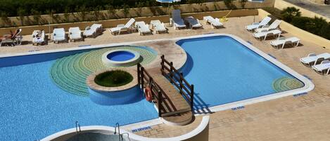 Zona de piscina con múltiples tumbonas, un trampolín y un flotador.