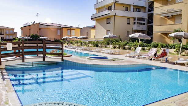 Une piscine entourée d’une terrasse en bois, de chaises longues et de parasols.