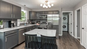 Una cocina moderna con armarios oscuros, un refrigerador de acero inoxidable, un microondas y un horno empotrado. Hay una isla grande con taburetes y una ventana sobre el fregadero.