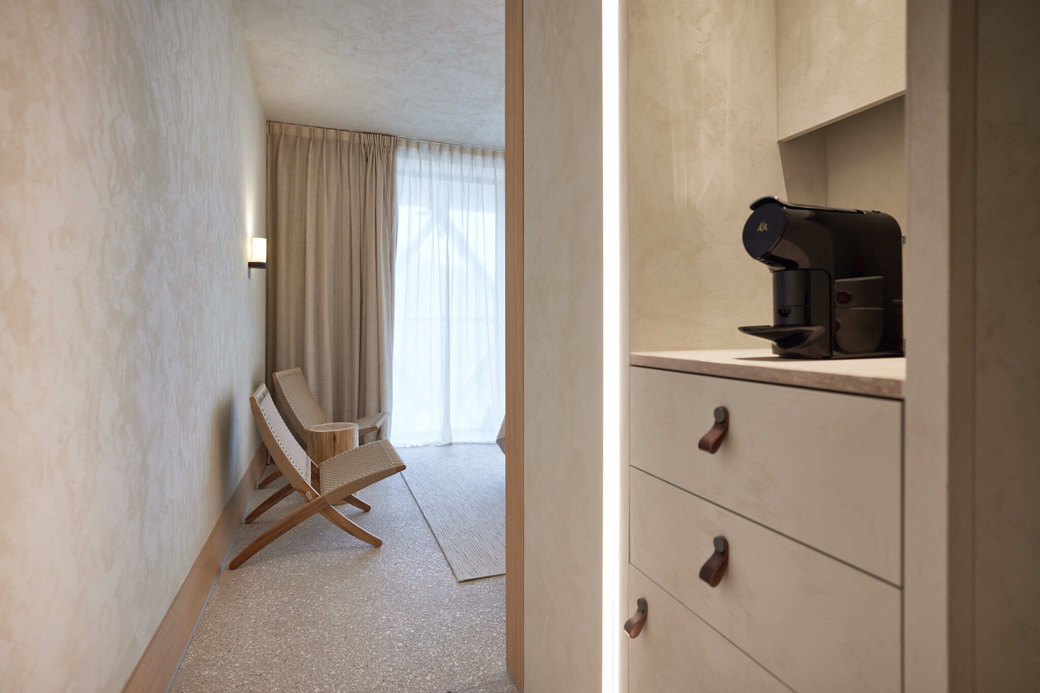 A hotel room with a wooden chair, a small desk, and a minibar.