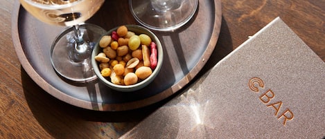 A tray with two glasses of white wine, a bowl of nuts, and a napkin with a logo.