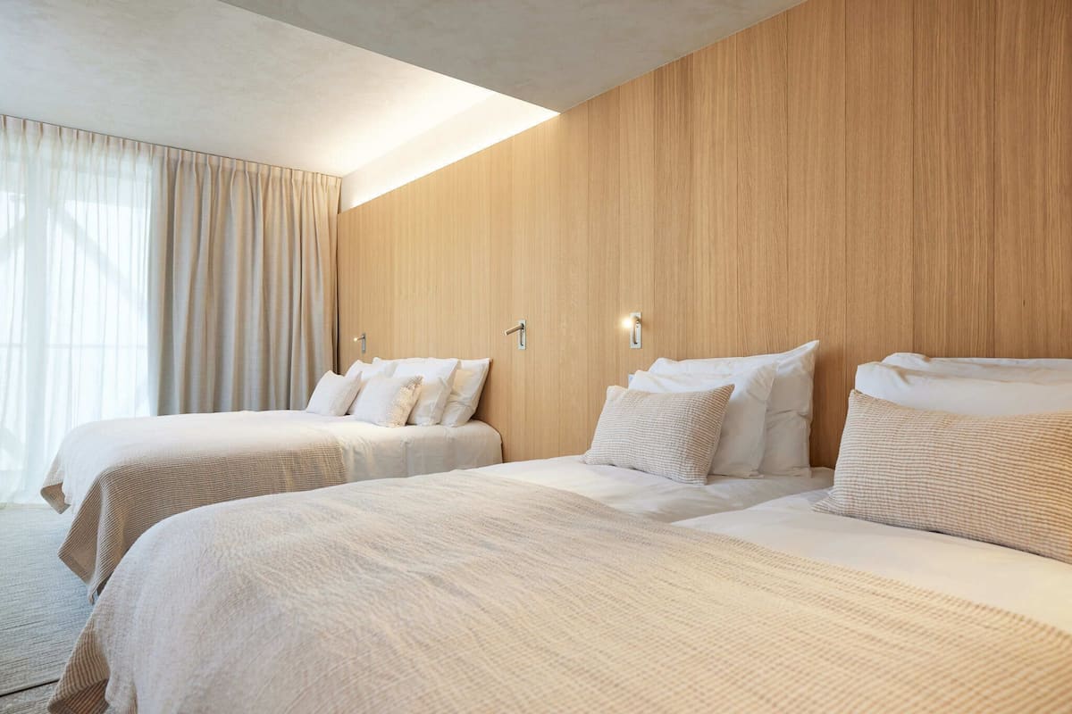 Ein Hotelzimmer mit zwei Betten, einer Holzwand und einem großen Fenster mit Vorhängen.