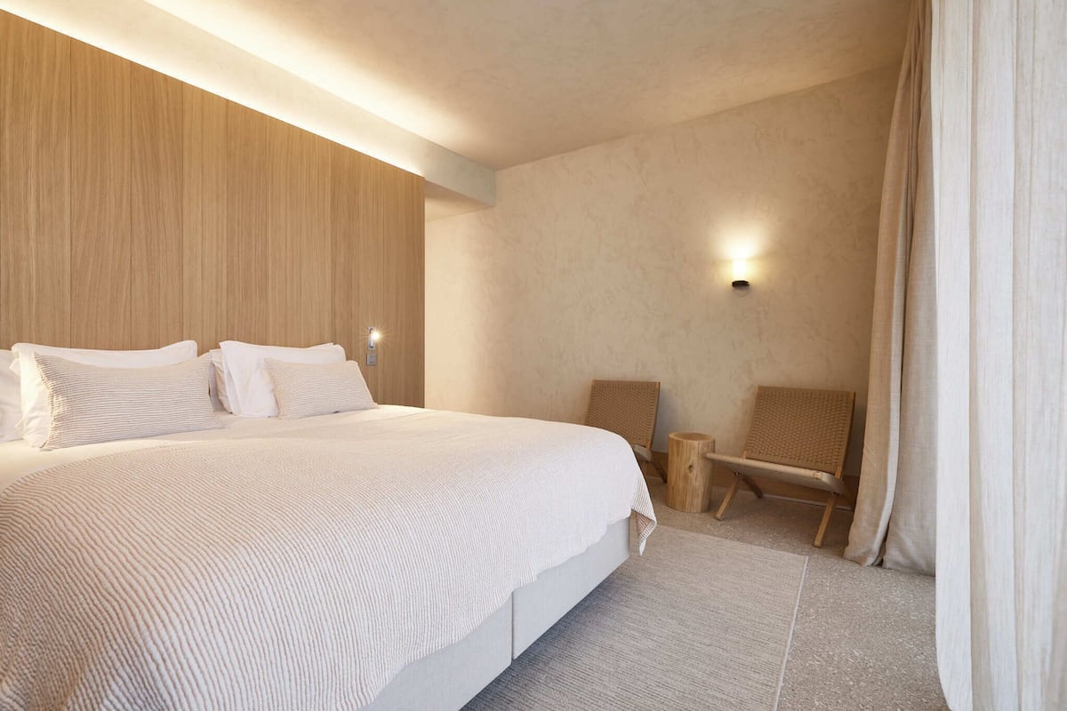 Ein modernes Hotelzimmer mit einem großen Bett, einer Wand in Holzoptik, einem kleinen Holzstuhl und einer Wandleuchte.