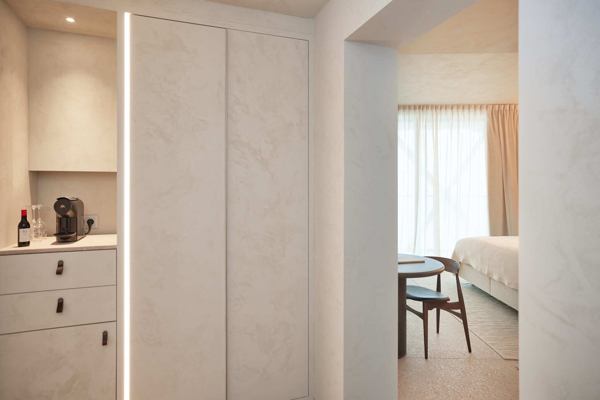 Een hotelkamer met een bed, een klein tafeltje met stoel, een minibars kast.