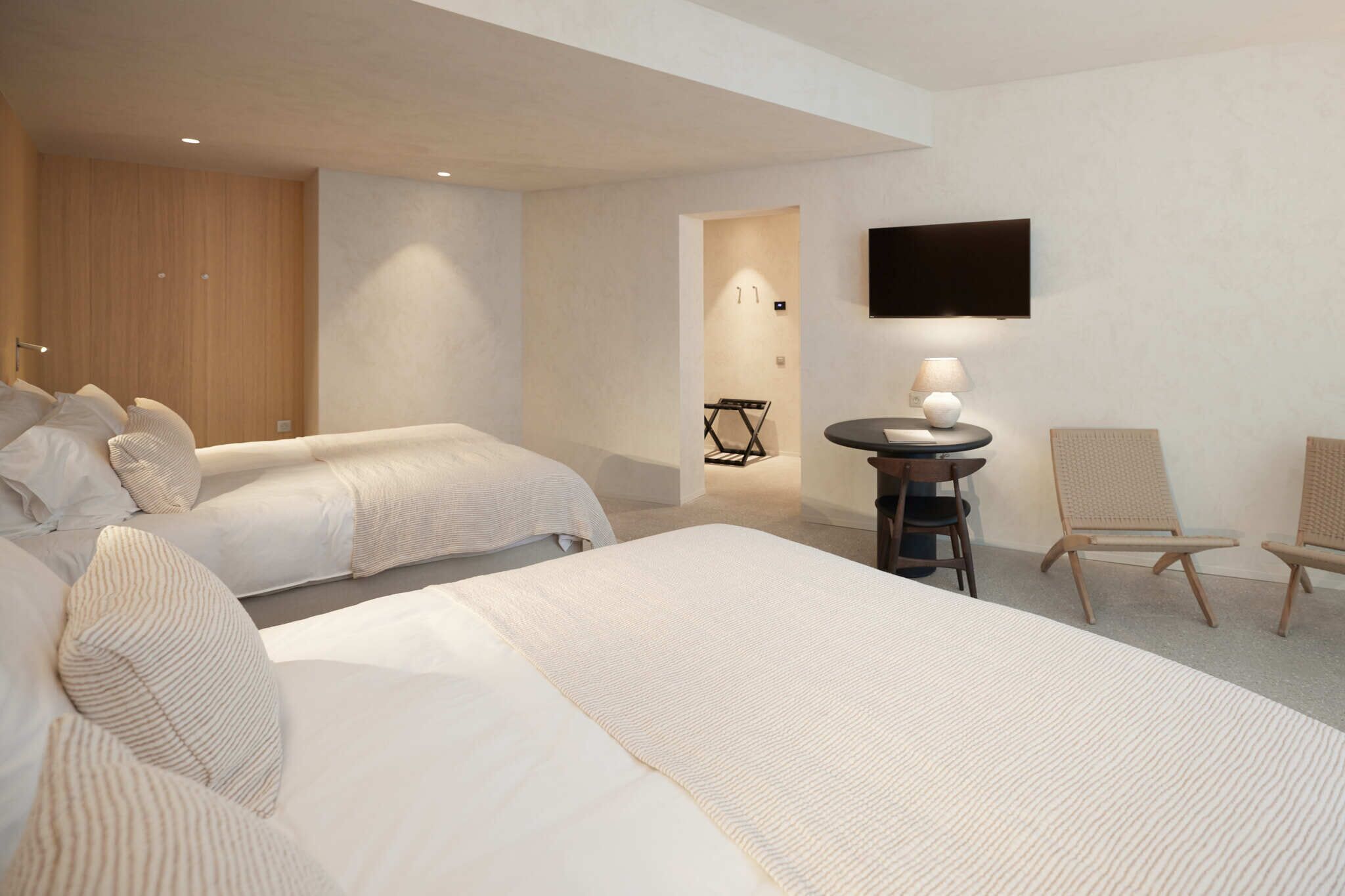 Een moderne hotelkamer met twee bedden, een flatscreentelevisie, een klein tafeltje met een lamp en twee stoelen.