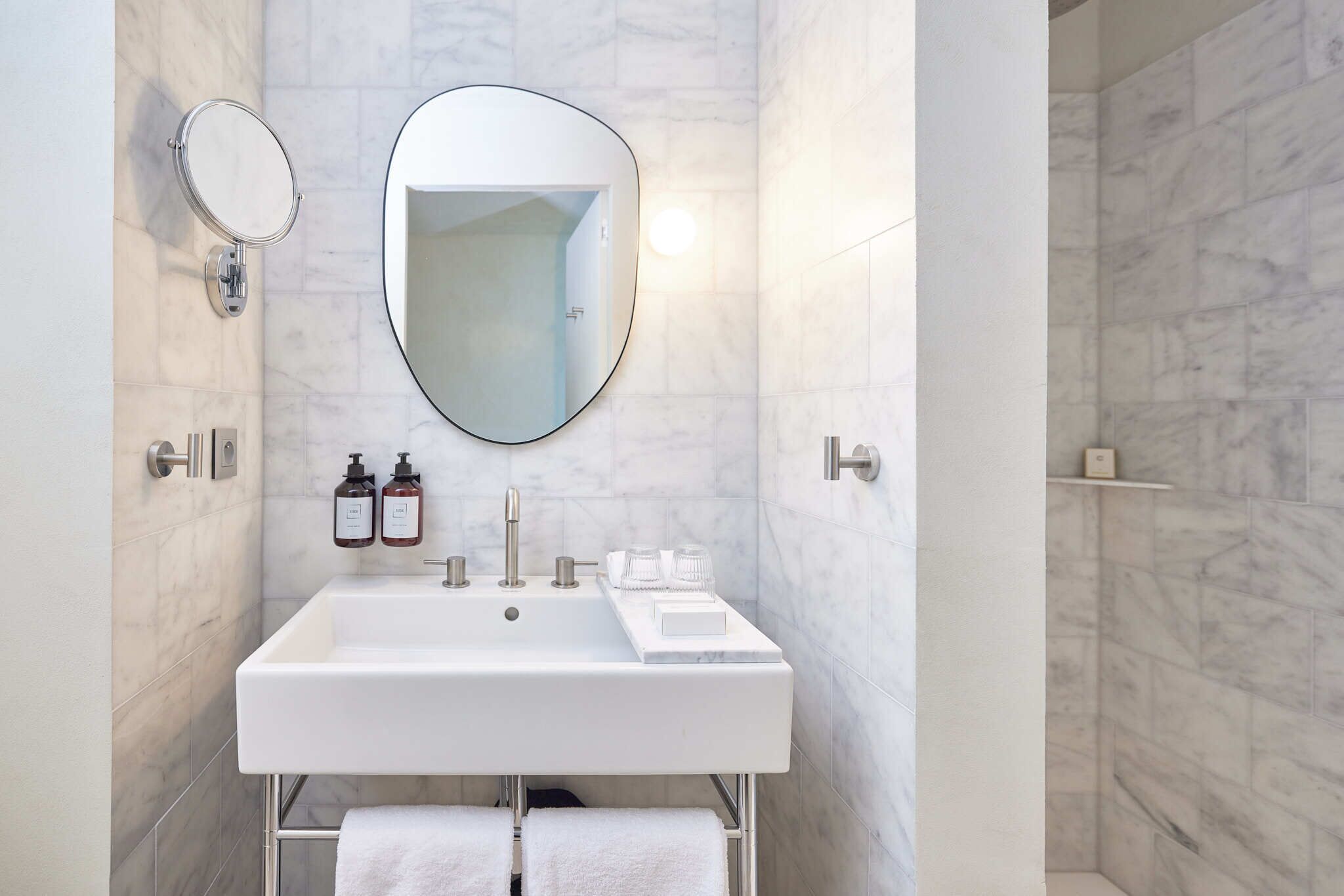 A modern bathroom with a white sink, two mirrors, and a large mirror above the sink.