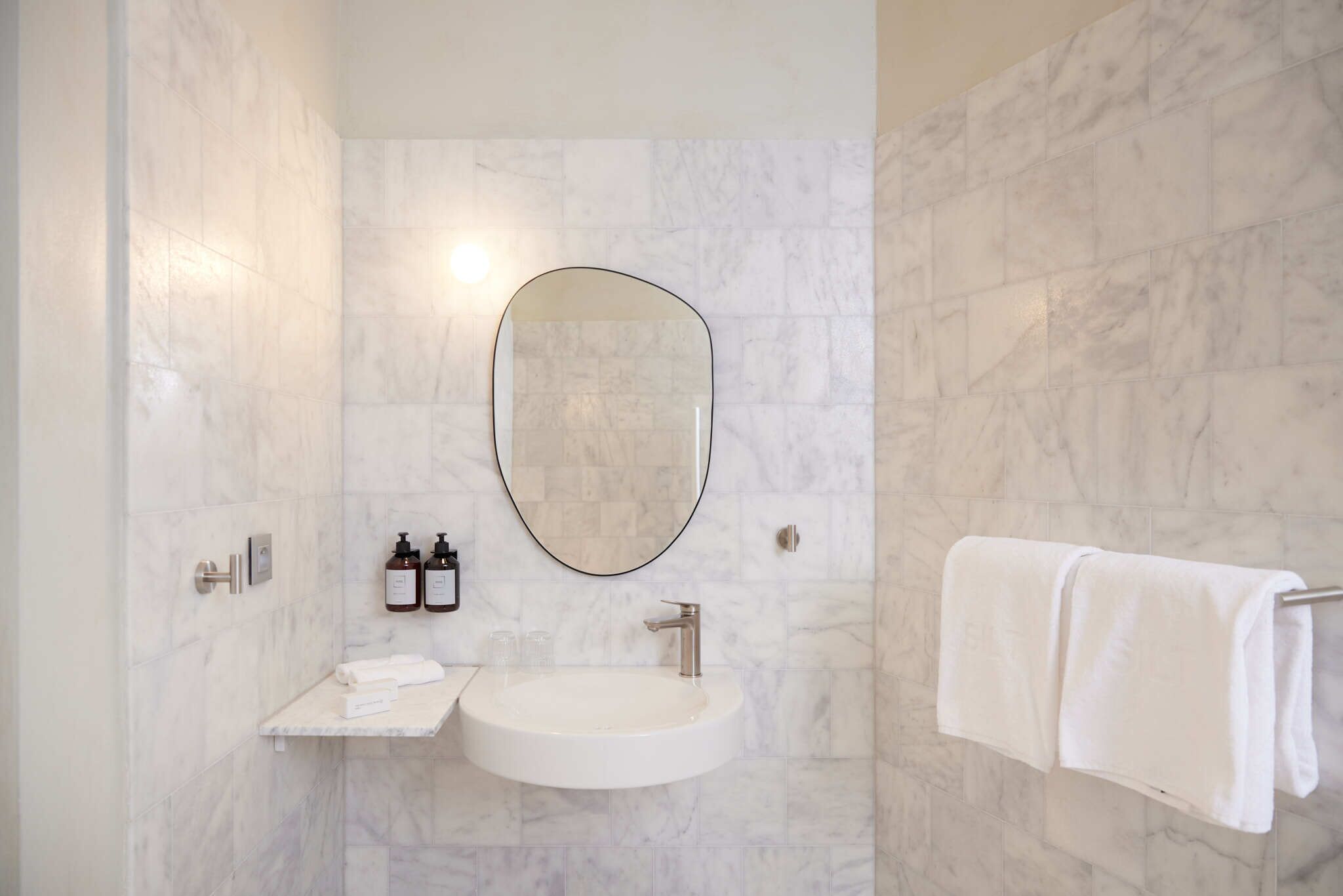 Un baño con pared de mármol, un espejo redondo, un lavamanos y un perchero para toallas.