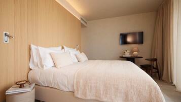 A hotel room with a bed, a bedside table, a lamp, a TV, and a small table with decorative items.