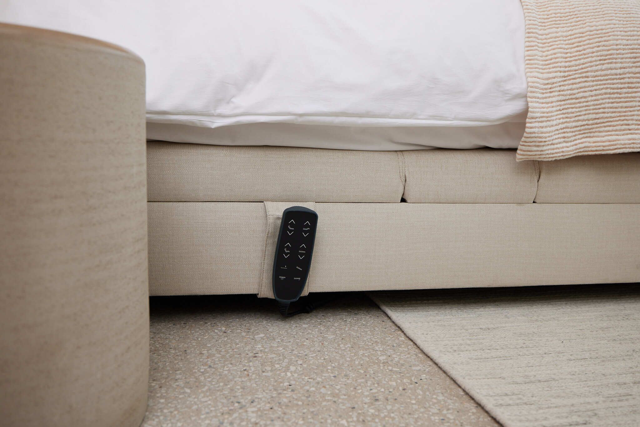 A remote control on a beige sofa with a white pillow and a beige blanket.