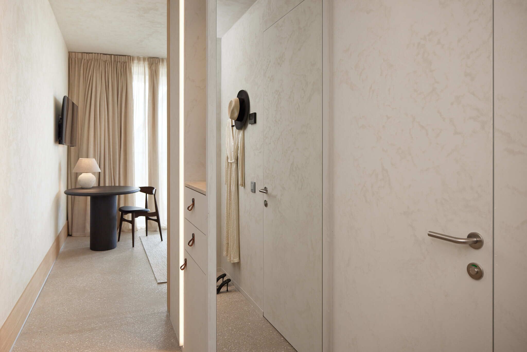 Una habitación de hotel con cama, escritorio con silla, televisor montado en la pared y puerta con toalla colgada.