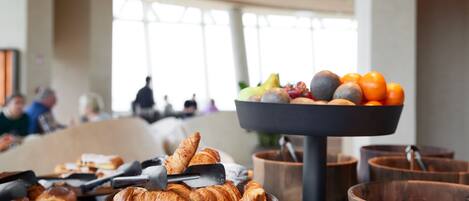 A breakfast buffet with croissants, fruits, and oranges.
