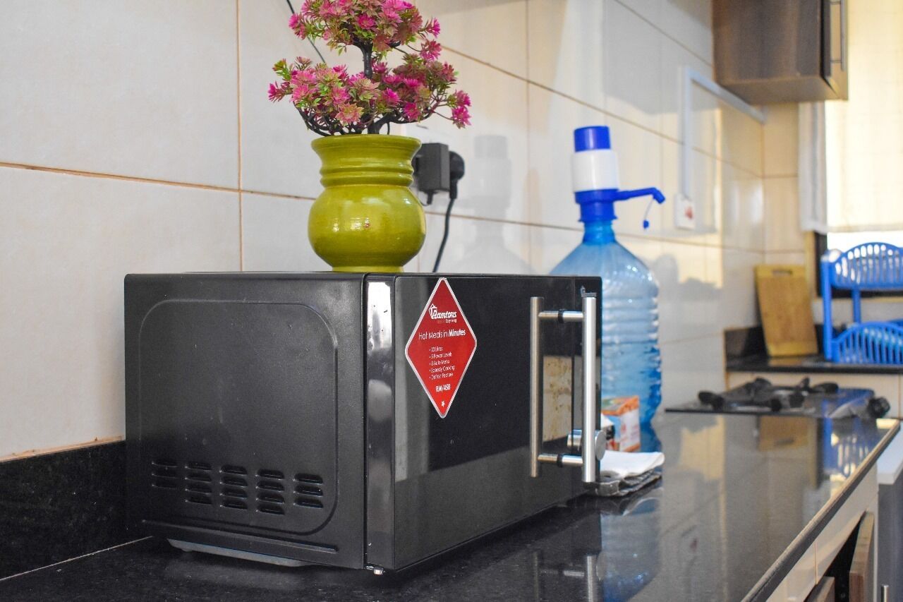 Una cocina con microondas, un florero verde con flores rosadas y un dispensador de agua azul sobre la encimera.