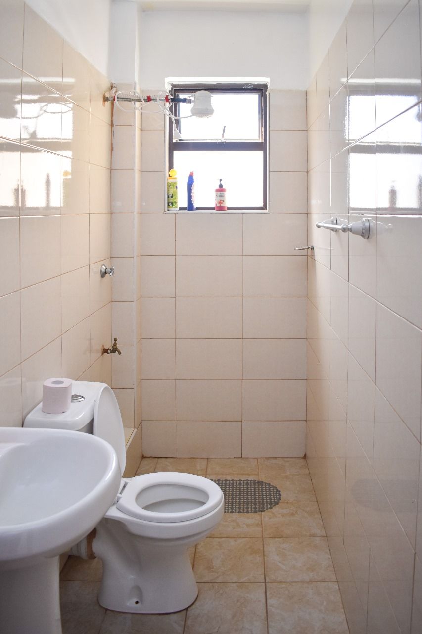 A small bathroom with a toilet, sink, and a window above the shower.