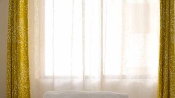 Una habitación con una cama, una ventana con cortinas translúcidas y una barra para cortinas.