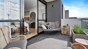 A modern balcony with wicker furniture, a glass door leading to an interior space, and a view of the cityscape. - Cityscape at The Elliott in the Heart of Hobart (Hobart)