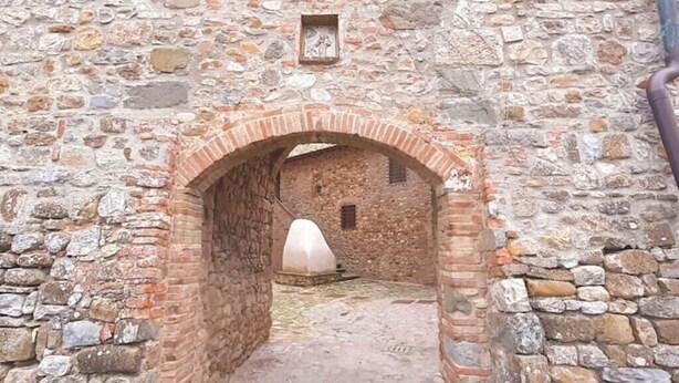 Un arco in pietra che dà accesso a un cortile con una piccola costruzione bianca in fondo.