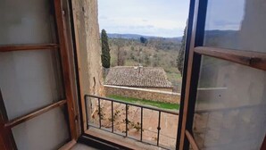 Un balcone con ringhiera in metallo che si affaccia su un paesaggio rurale con alberi e un edificio.