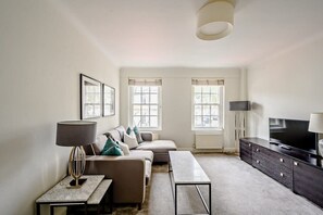Ein modernes Wohnzimmer mit einer Couch, einem Couchtisch, einem Fernseher und einer Lampe.