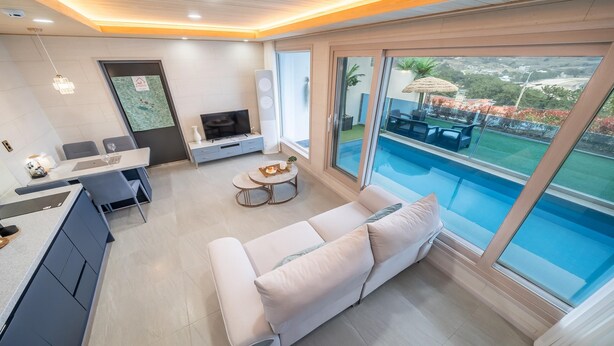 Ein modernes Wohnzimmer mit Sofa, Essbereich, Fernseher und Blick auf einen Swimmingpool.