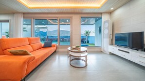Ein modernes Wohnzimmer mit einer Couch, einem Couchtisch, einem Fernseher und großen Fenstern mit Blick auf einen Pool und Berge.