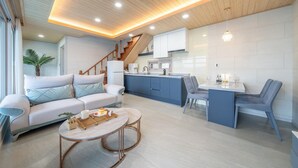 Ein modernes Wohnzimmer mit Sofa, Couchtisch und Essbereich mit Stühlen sowie einer Küche im Hintergrund.
