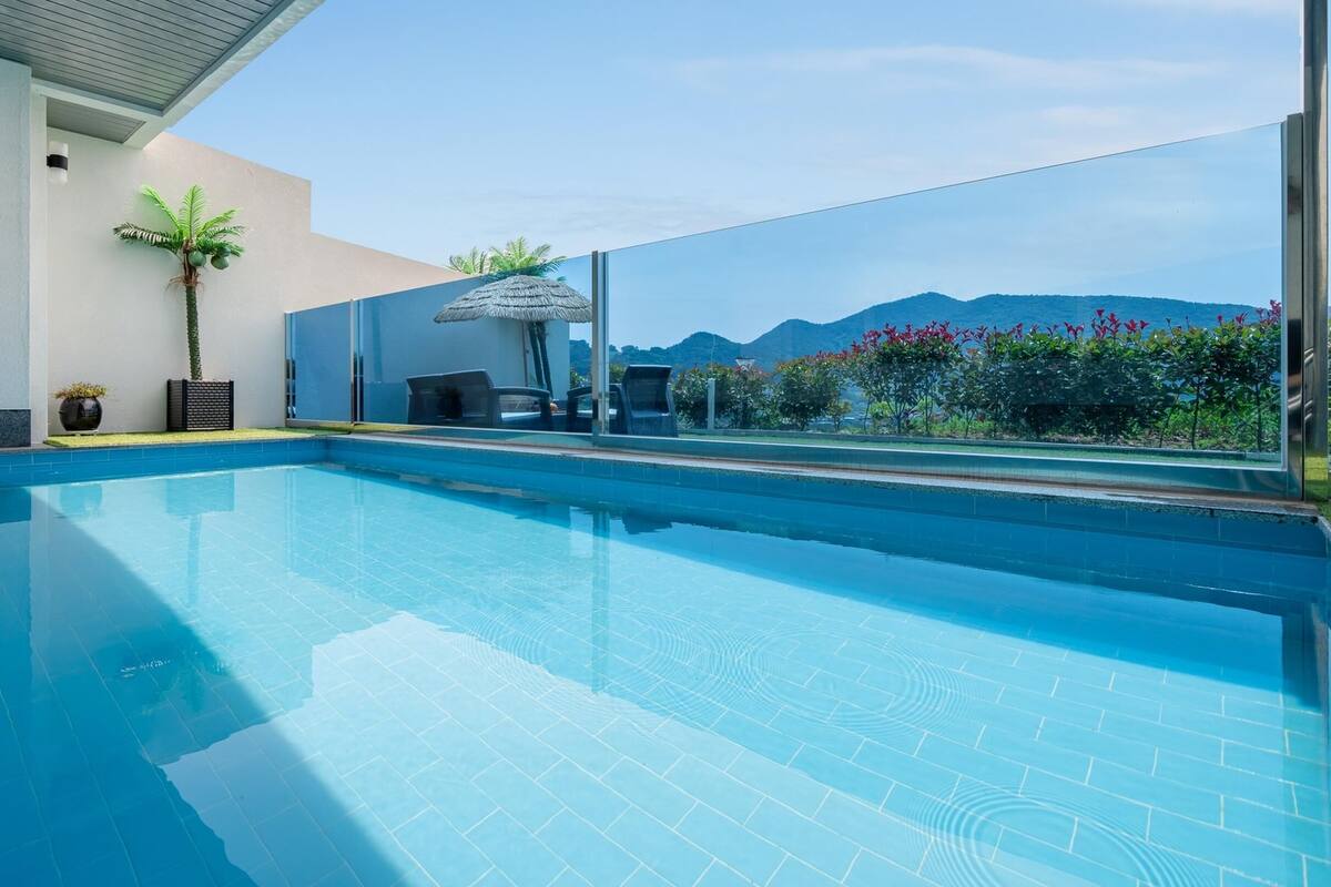 Una piscina interior con agua cristalina azul, rodeada por un muro de cristal que ofrece vistas a montañas y flores.