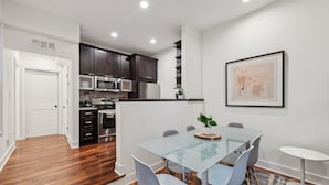 Una cocina moderna con armarios oscuros, electrodomésticos de acero inoxidable y una mesa de comedor de vidrio con sillas.