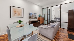Una sala de estar moderna con una mesa de comedor de vidrio, un sofá gris, un aparador de madera y un espejo grande.