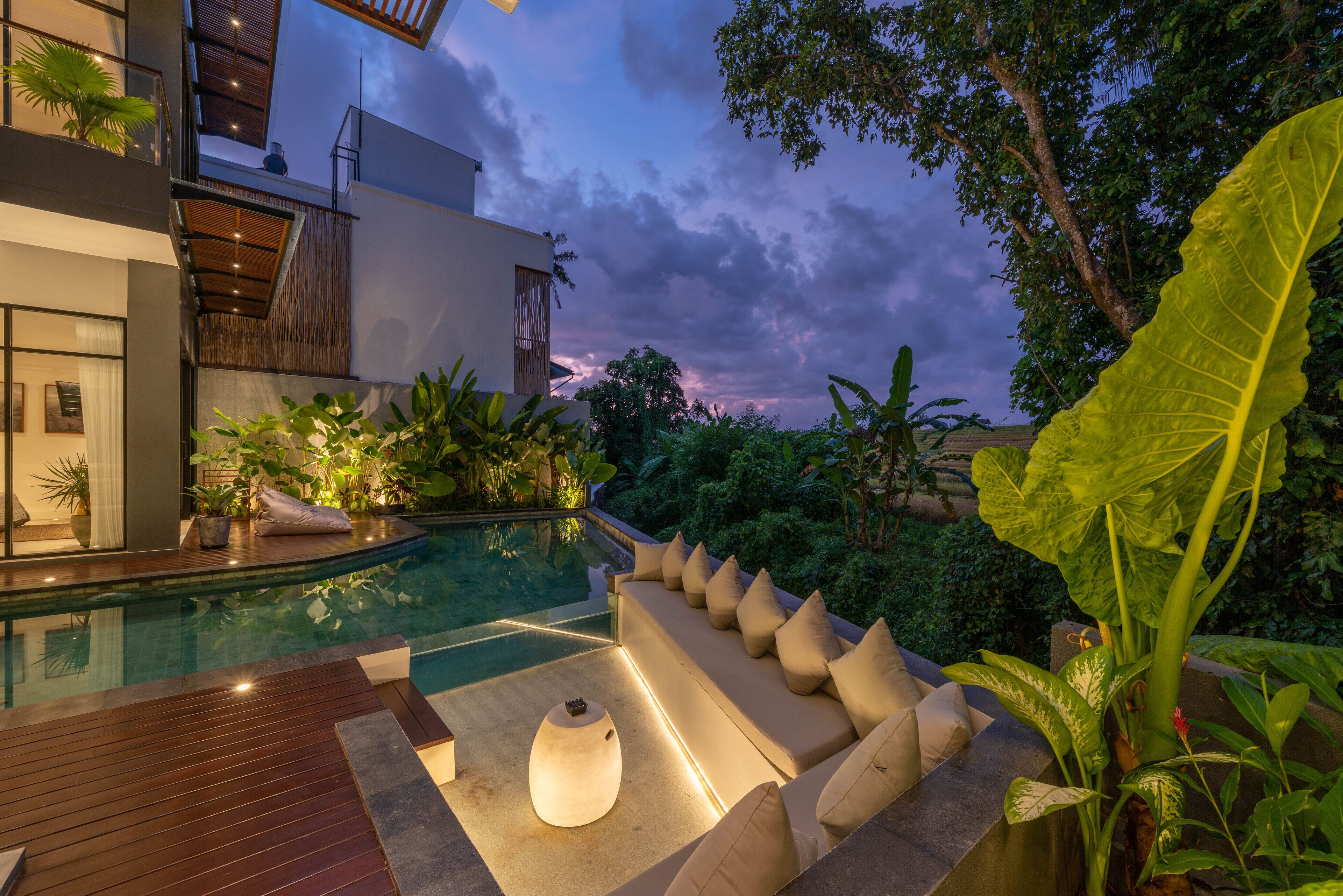 A modern outdoor pool area with a wooden deck, a built-in seating area, and lush greenery.