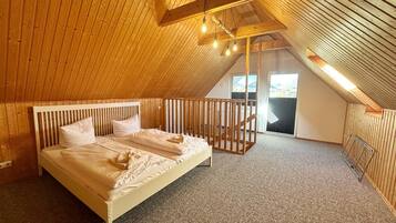 Ein Schlafzimmer mit schrägen Wänden, einem Bett und Blick ins Freie durch ein Fenster.
