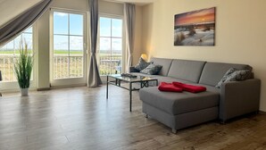 En moderne stue med en grå sofa, et lille sofabord og udsigt over landskabet gennem store vinduer.