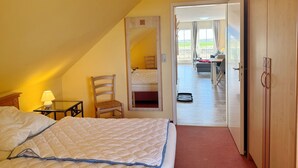 Et soveværelse med en seng, en stol, et natbord og et spejl. En dør fører ud til en balkon med et bord og stole.