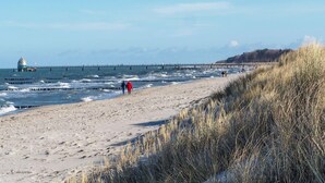 Une plage avec une jetée qui s’avance dans l’eau, une structure en forme de dôme et des personnes qui se promènent le long du rivage.