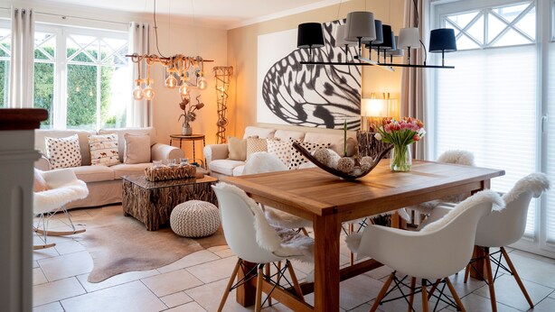 Un salon moderne avec une table à manger en bois, des chaises blanches, un canapé et un grand tableau abstrait accroché au mur.