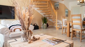 Una sala de estar moderna con una escalera de madera, un televisor de pantalla plana, una mesa de centro con revistas y una zona de estar acogedora.