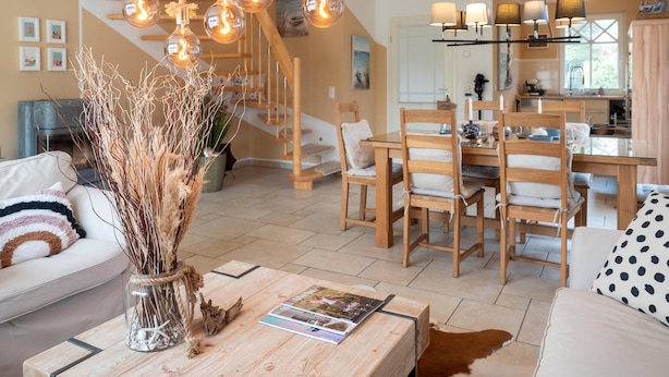Una sala moderna con una mesa de comedor de madera, un sofá y una mesa de centro con revistas. Una escalera con barandilla de madera conduce a un piso superior.