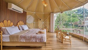 Habitación tipo tienda con cama, suelo de madera y vistas amplias por las ventanas.
