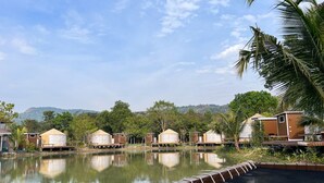 Una vista tranquila de un lago con bungalows sobre el agua, cielo despejado y abundante vegetación.