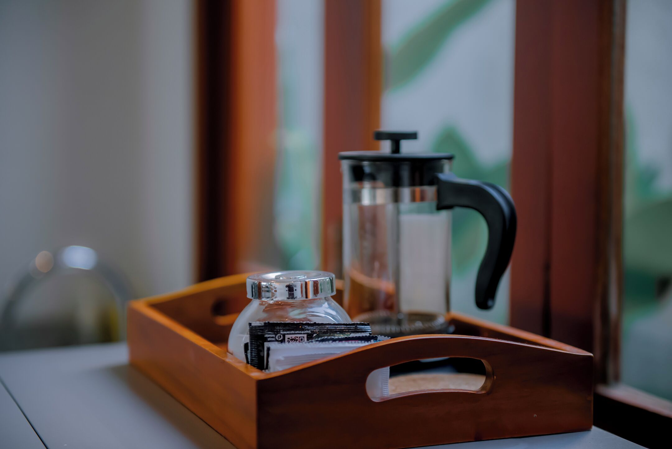 A wooden tray with a coffee maker and a glass container on a table.