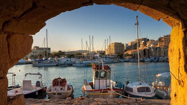 A marina with boats docked, a clear sky, and buildings in the background.