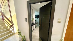 A modern interior with a staircase, a dark door leading to a kitchen, and potted plants.