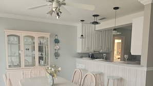 A dining area with a white table and chairs, a ceiling fan, and a kitchen area with cabinets and a countertop.