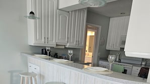 A kitchen with a marble countertop, wooden stools, and white cabinetry.