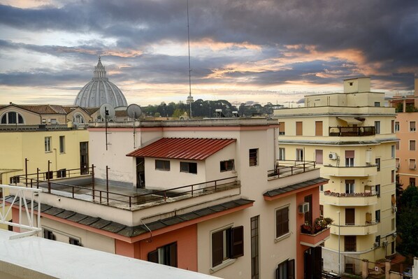 A multi-story building with balconies, a dome structure in the background, and a clear sky.