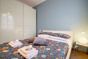 A bed with floral bedding, a bedside table with a lamp, and a wall with a light switch.